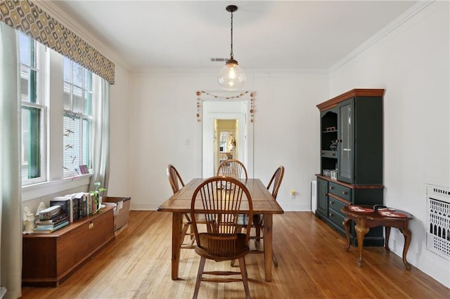 dining area featuring visible vents, baseboards, light wood-type flooring, ornamental molding, and heating unit