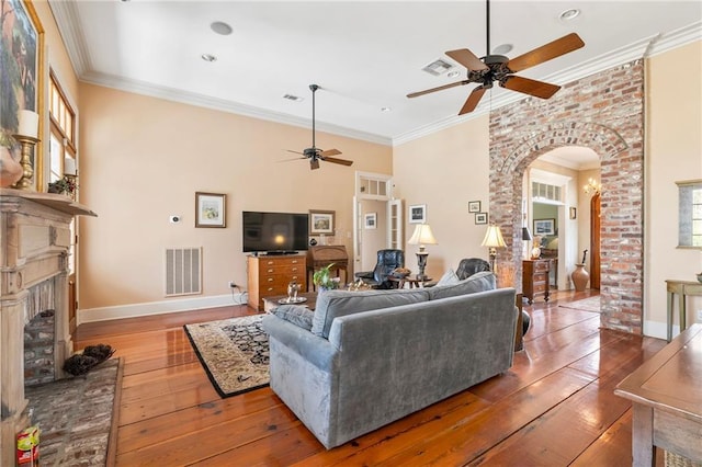 living room featuring ornamental molding, a fireplace with raised hearth, visible vents, and arched walkways