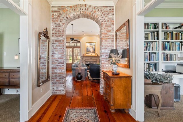 hallway with crown molding, hardwood / wood-style flooring, built in features, and arched walkways