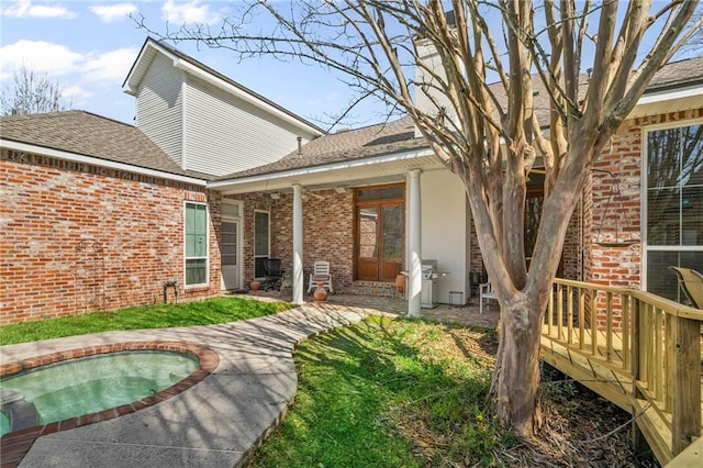 back of house featuring an in ground hot tub, brick siding, and a shingled roof