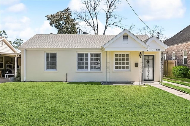 view of front of property with stucco siding, a front lawn, and a shingled roof