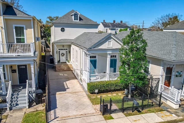 view of front of house featuring a fenced front yard, a balcony, covered porch, and roof with shingles