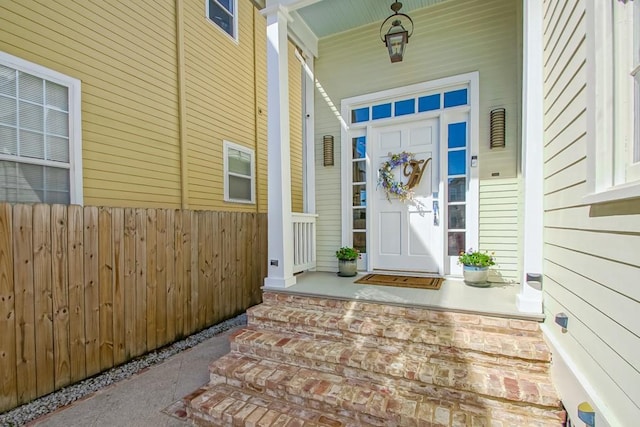 doorway to property with covered porch and fence