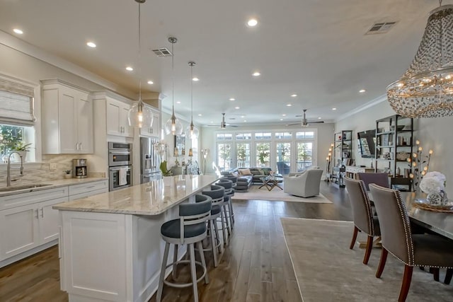 kitchen featuring a healthy amount of sunlight, visible vents, a sink, crown molding, and a center island