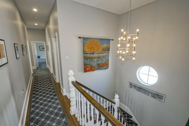 corridor with an upstairs landing, a chandelier, baseboards, and wood finished floors