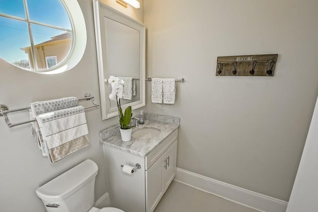 half bath featuring toilet, vanity, and baseboards