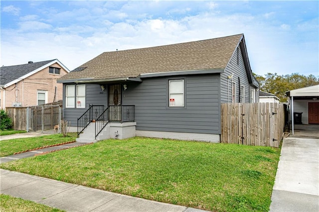 view of front facade with a shingled roof, driveway, fence, and a front lawn