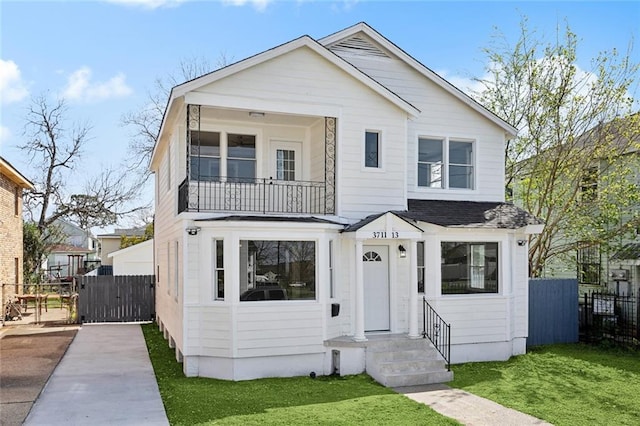 view of front of house with a balcony, a front yard, and fence