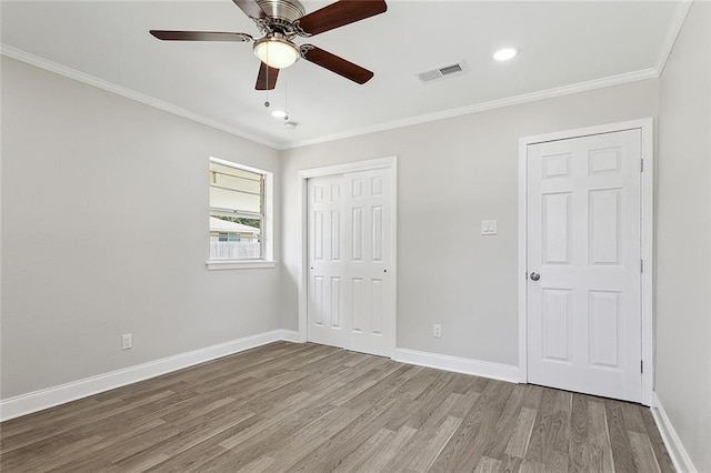 unfurnished bedroom featuring visible vents, baseboards, wood finished floors, and crown molding