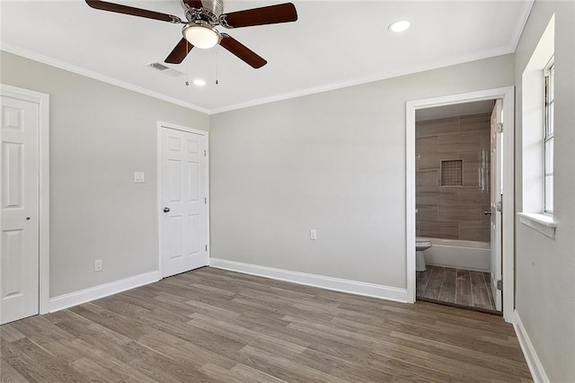 unfurnished bedroom featuring visible vents, crown molding, baseboards, wood finished floors, and ensuite bath