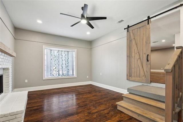 unfurnished living room featuring visible vents, a barn door, a fireplace, wood finished floors, and a ceiling fan