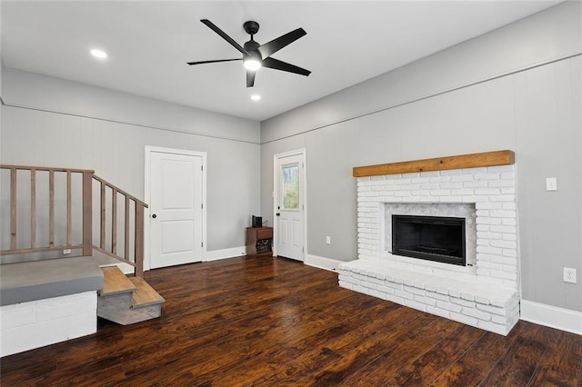 unfurnished living room featuring stairway, baseboards, ceiling fan, hardwood / wood-style flooring, and a brick fireplace