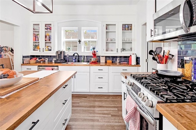 kitchen featuring a sink, wood counters, white cabinetry, stainless steel appliances, and light wood finished floors