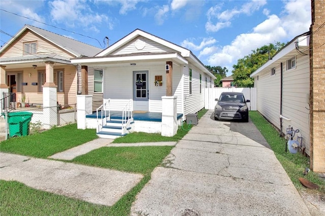 shotgun-style home with a porch, concrete driveway, and fence