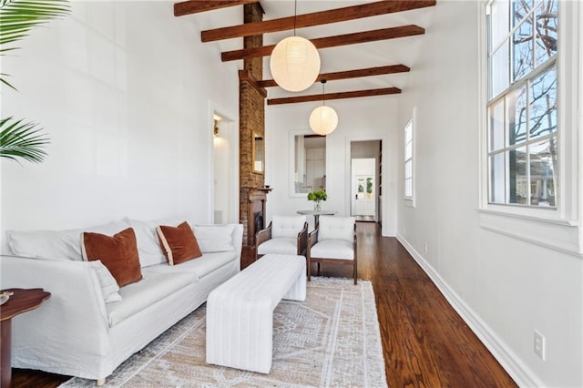 living room with beamed ceiling, a brick fireplace, baseboards, and wood finished floors