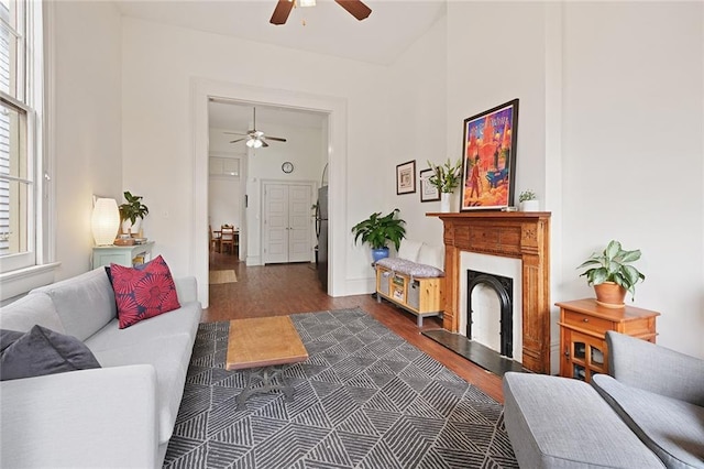 living room featuring a fireplace with raised hearth, ceiling fan, and wood finished floors