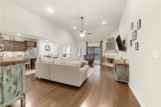 living area featuring arched walkways, a fireplace, ceiling fan, dark wood-style flooring, and vaulted ceiling