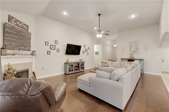 living area featuring vaulted ceiling, a fireplace, baseboards, and wood finished floors