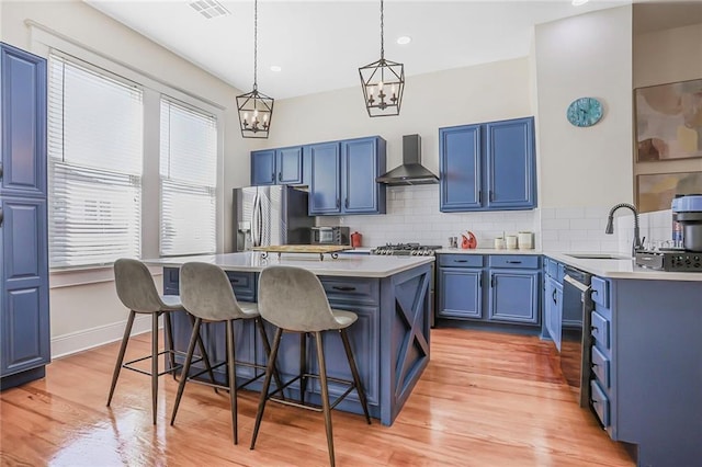 kitchen featuring a sink, stainless steel appliances, blue cabinets, and wall chimney range hood