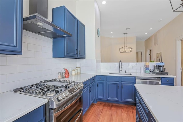 kitchen featuring blue cabinetry, decorative backsplash, appliances with stainless steel finishes, wall chimney exhaust hood, and a sink