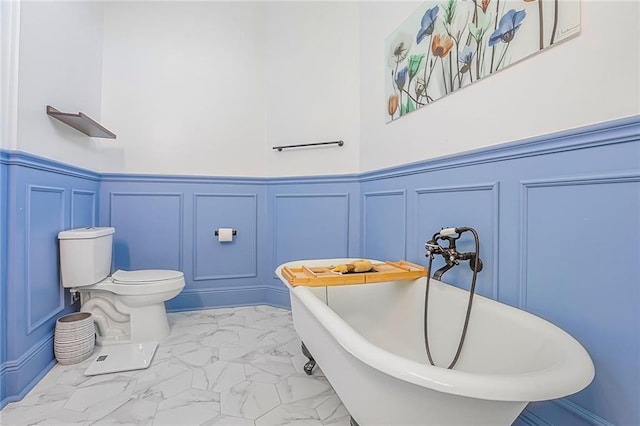 full bath featuring a wainscoted wall, marble finish floor, a freestanding bath, and toilet