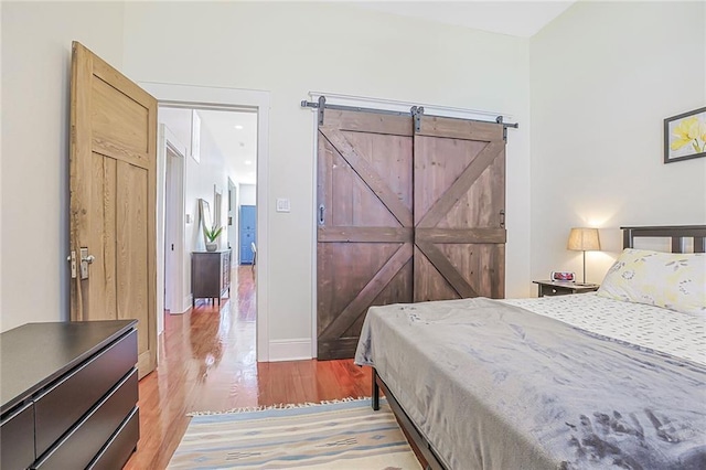 bedroom featuring light wood-style flooring, baseboards, and a barn door