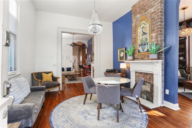 dining room featuring arched walkways, ceiling fan with notable chandelier, a brick fireplace, and wood finished floors