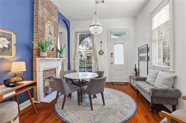 dining space with visible vents, a brick fireplace, an inviting chandelier, and wood finished floors