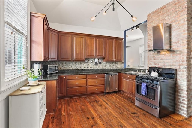 kitchen with dark wood-style floors, a sink, stainless steel appliances, wall chimney exhaust hood, and tasteful backsplash