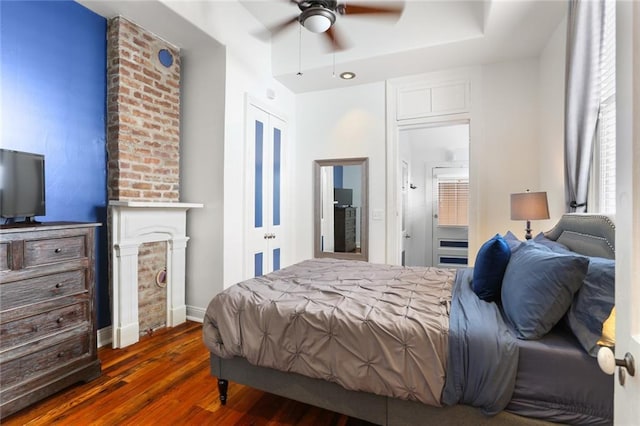 bedroom featuring a ceiling fan, baseboards, ensuite bath, a fireplace, and dark wood-type flooring