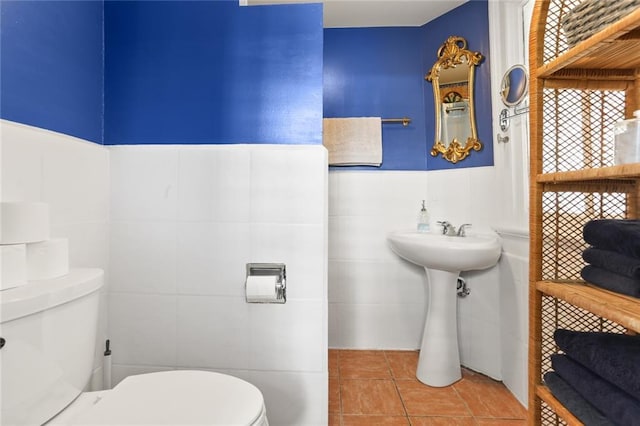 half bath with tile walls, toilet, tile patterned floors, and a sink