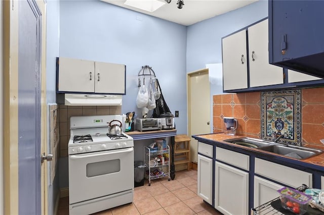 kitchen featuring white range with gas cooktop, under cabinet range hood, a sink, tasteful backsplash, and white cabinets