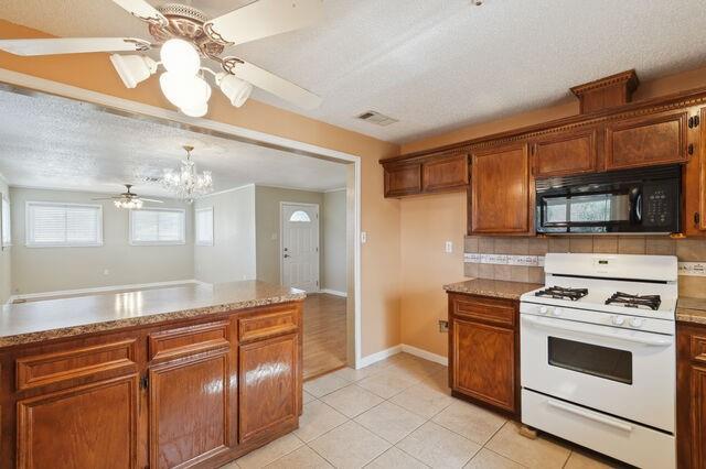 kitchen featuring light tile patterned floors, visible vents, white range with gas cooktop, black microwave, and ceiling fan with notable chandelier