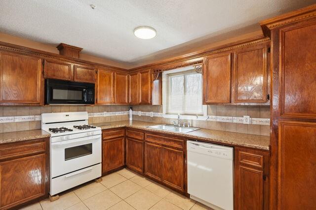 kitchen featuring a sink, white appliances, brown cabinetry, and light tile patterned floors