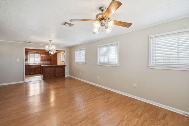 unfurnished living room featuring light wood-type flooring, visible vents, baseboards, and ceiling fan with notable chandelier