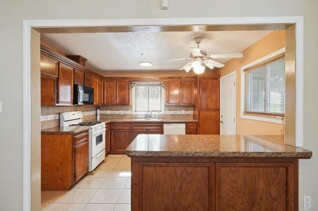 kitchen with brown cabinetry, a peninsula, light tile patterned flooring, white appliances, and a sink