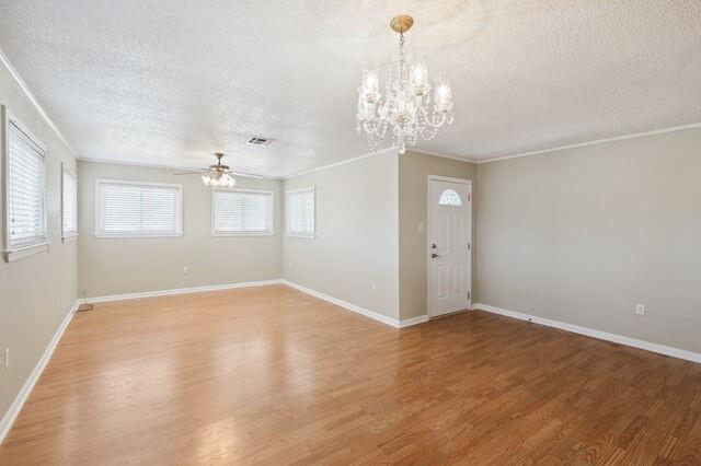 empty room with light wood-style flooring, ceiling fan with notable chandelier, baseboards, and a textured ceiling