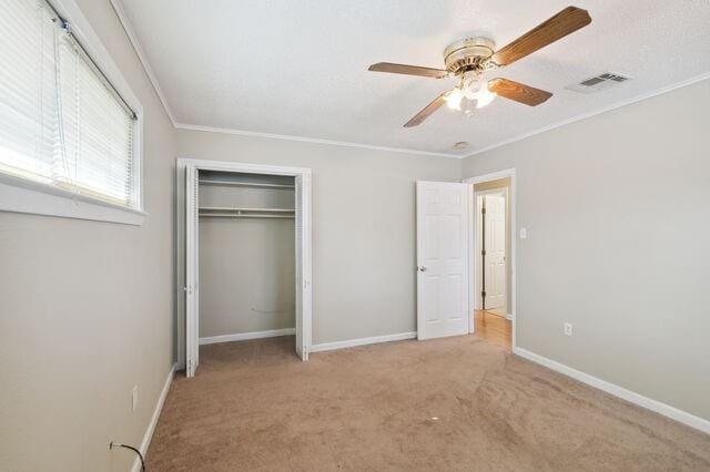 unfurnished bedroom featuring visible vents, crown molding, baseboards, carpet flooring, and a closet