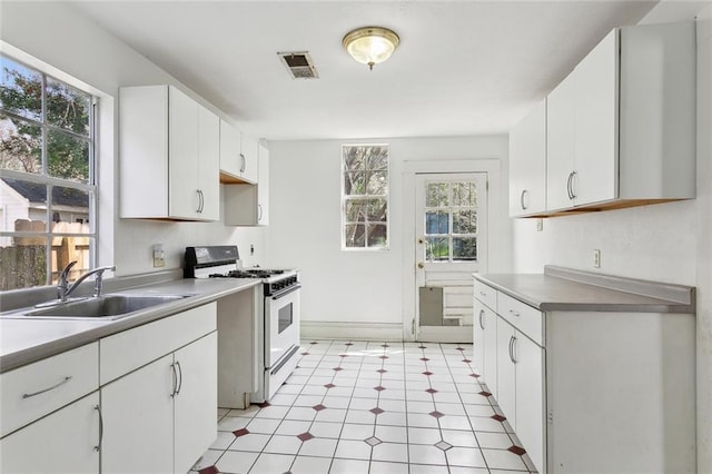 kitchen with visible vents, white range with gas stovetop, a sink, light countertops, and white cabinetry