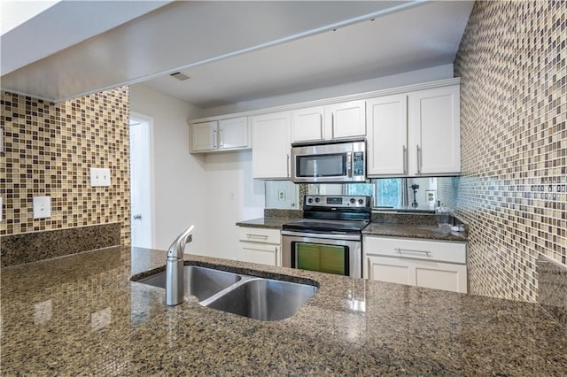 kitchen with a sink, backsplash, stainless steel appliances, dark stone counters, and white cabinets