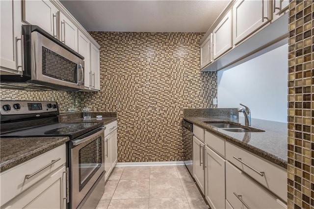 kitchen featuring tile walls, dark stone counters, light tile patterned floors, stainless steel appliances, and a sink