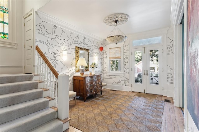 entryway with crown molding, wallpapered walls, stairs, and wood finished floors