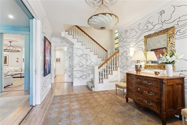 entryway featuring hardwood / wood-style flooring, an inviting chandelier, crown molding, wallpapered walls, and stairs