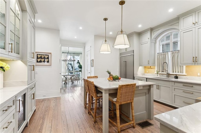 kitchen with light stone counters, a sink, built in refrigerator, pendant lighting, and light wood-type flooring