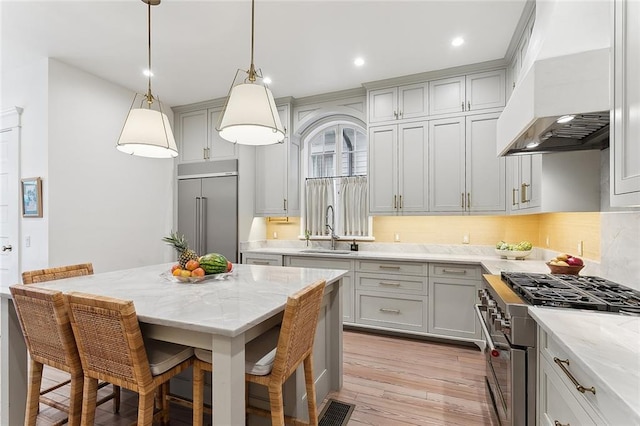 kitchen featuring light wood-type flooring, a sink, premium appliances, a breakfast bar area, and extractor fan