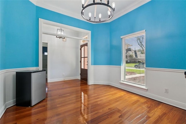 unfurnished dining area with baseboards, wood finished floors, a chandelier, and ornamental molding