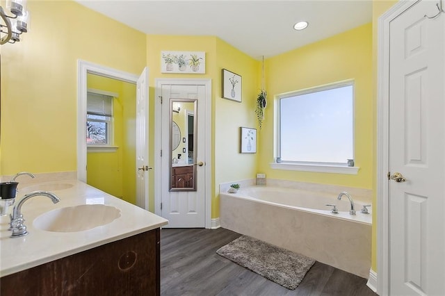 full bath with double vanity, wood finished floors, a bath, and a sink