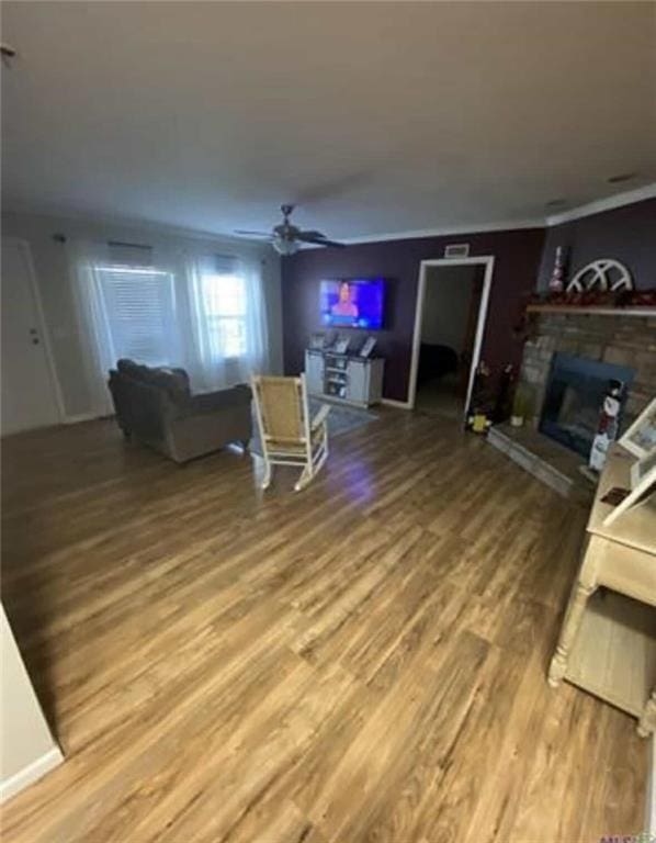 living area with a fireplace, crown molding, wood finished floors, and a ceiling fan