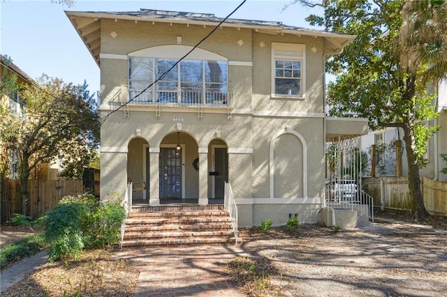 view of front facade featuring a porch, a balcony, fence, and stucco siding