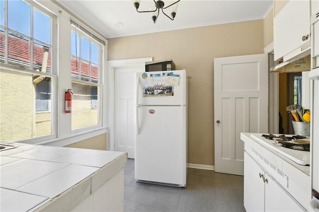 kitchen featuring white appliances, white cabinets, crown molding, baseboards, and a chandelier